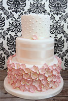 Pink wedding cake covered with pink sugar flowers and satin ribbon.